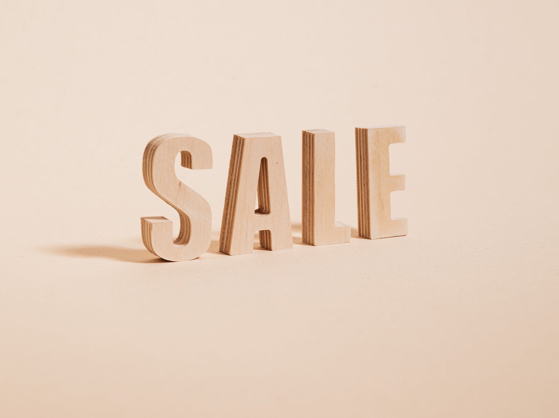 Image of the word sale in all caps, made out of wood, on a background of light beige. 