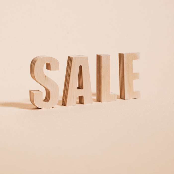 Image of the word sale in all caps, made out of wood, on a background of light beige. 